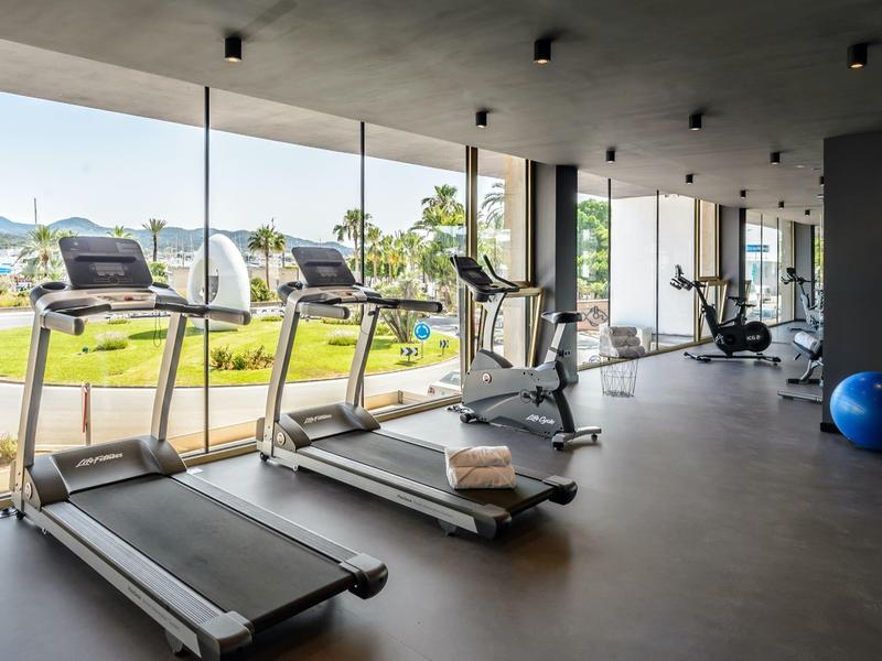 Jasna siłownia z bieżniami i sprzętem obok dużych okien.