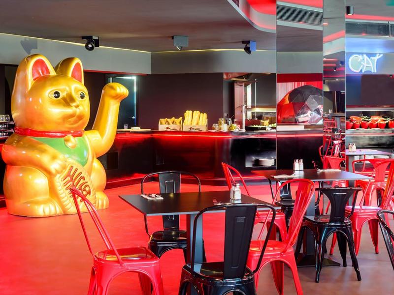 Czerwony pokój z czarnymi meblami i dużą złotą dekoracją kota machającego łapą.