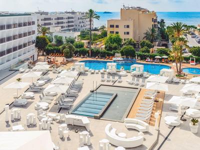 Piscina moderna dell'hotel con molte sdraio e ombrelloni bianchi sotto un cielo sereno.