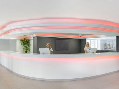 Moderner Empfangsbereich mit weißem Tresen und wellenförmiger Deckenbeleuchtung in sanftem Rosa.