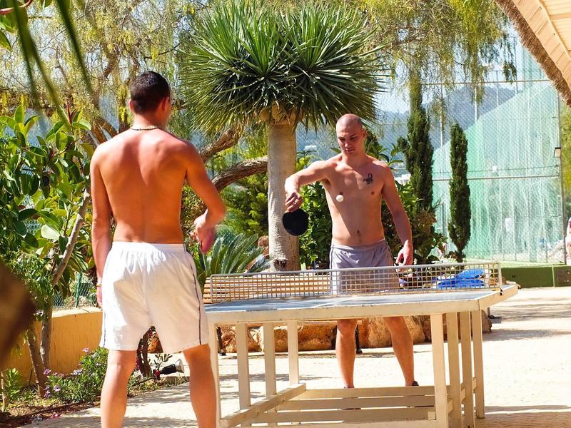 Twee mannen spelen tafeltennis in een hotel tuin op een zonnige dag.