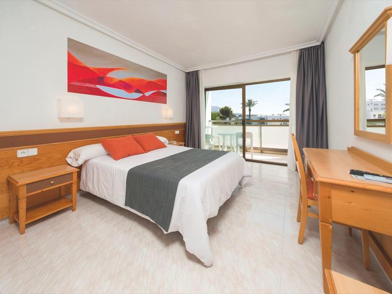 Lichte hotelkamer met tweepersoonsbed, houten meubels en balkon met uitzicht op zee.