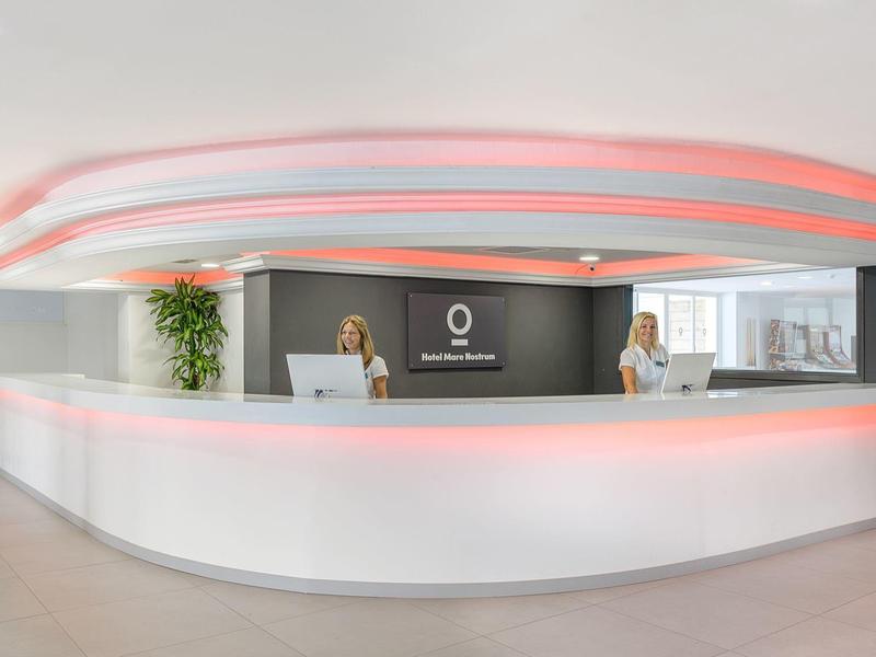 Moderne hotellobby met witte balie en verlichte plafondaccenten.