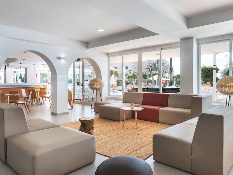 Lichte, moderne hotellounge met zitgroepen, tapijt en vloerlampen bij grote ramen.