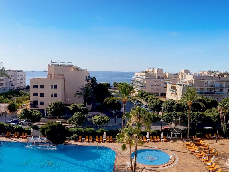 Hotel met zwembaden, palmbomen en zeezicht onder een heldere hemel.