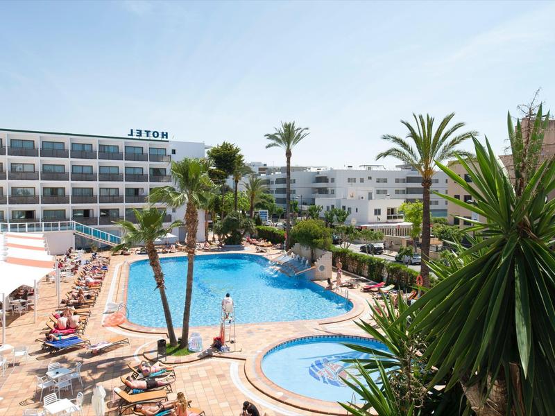 Hotelcomplex met meerdere zwembaden, palmbomen en ligstoelen onder een heldere hemel.