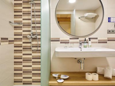 Baño moderno con lavabo, espejo y área de ducha con azulejos marrones y blancos.