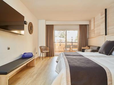 Habitación de hotel moderna con cama doble, televisor en la pared y acceso al balcón.