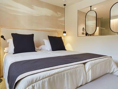 Habitación de hotel moderna con cama grande, almohadas blancas y azul oscuro y dos espejos redondos en la pared.