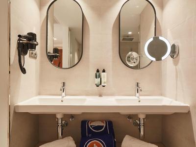 Baño moderno con dos lavabos, espejos redondos y secador de pelo en la pared.