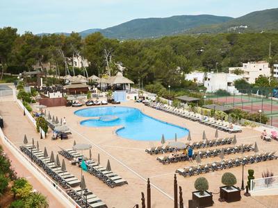 Gran piscina del hotel con tumbonas y sillas rodeada de árboles y montañas al fondo.