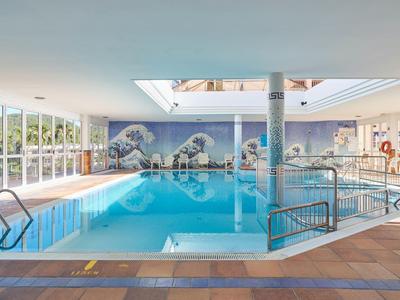 Piscina cubierta luminosa con grandes ventanales, muro de mosaico y escaleras cómodas para entrar.