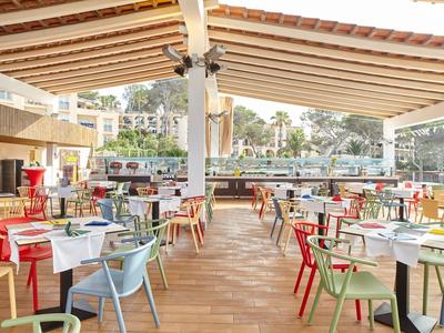 Área de restaurante abierta con sillas y mesas coloridas en terraza de madera bajo un toldo de madera.