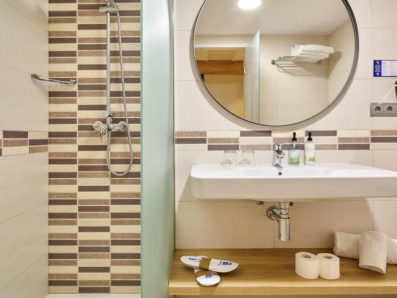 Baño moderno con lavabo, espejo y área de ducha con azulejos marrones y blancos.