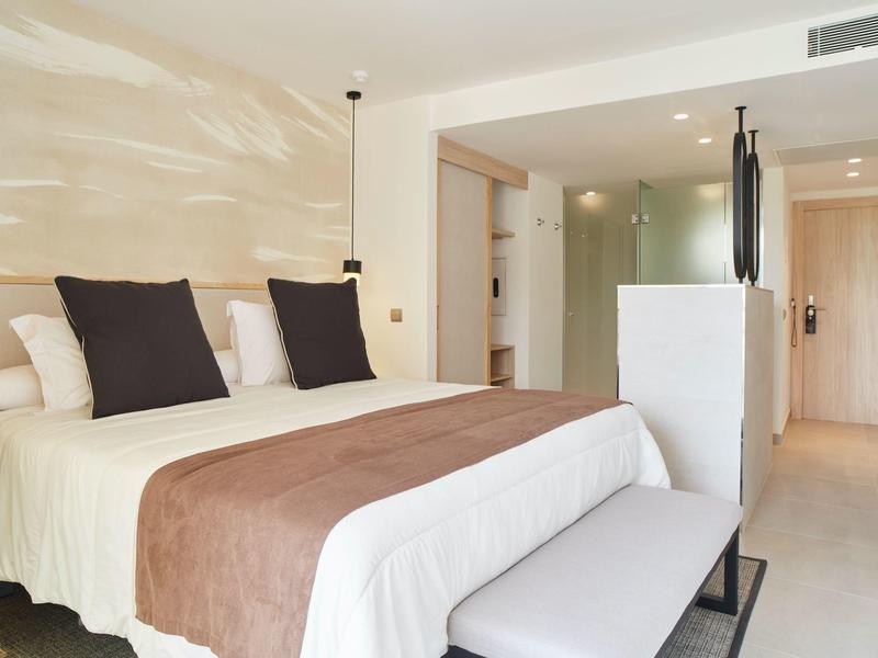 Habitación de hotel moderna con cama doble, ropa de cama blanca y marrón, y decoración minimalista.