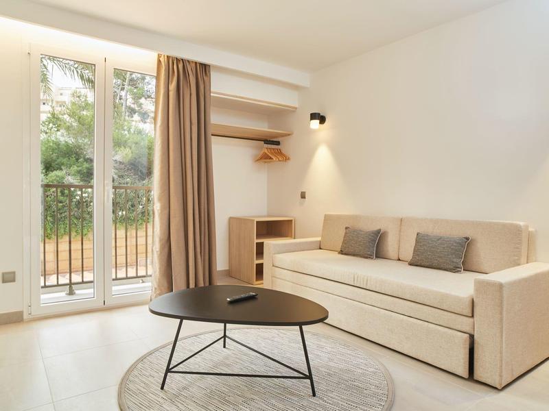 Sala luminosa con sofá beige, mesa de centro redonda y grandes ventanas con vista al verde.