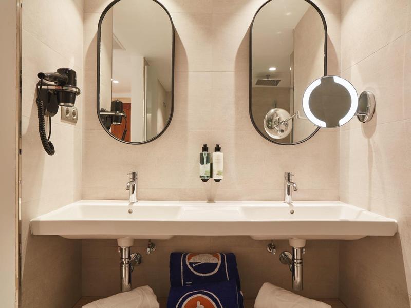 Baño moderno con dos lavabos, espejos redondos y secador de pelo en la pared.