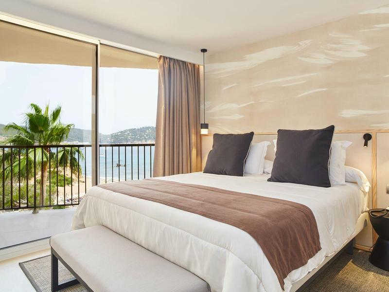 Moderna habitación de hotel con cama grande y balcón con vista al mar.