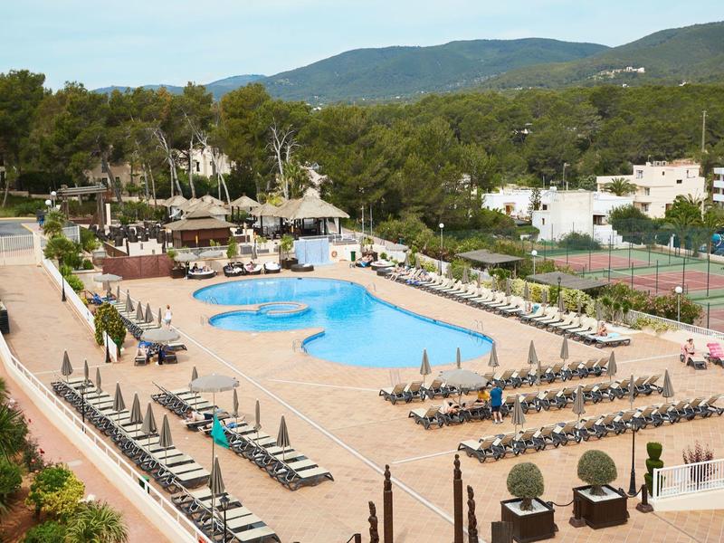 Gran piscina del hotel con tumbonas y sillas rodeada de árboles y montañas al fondo.