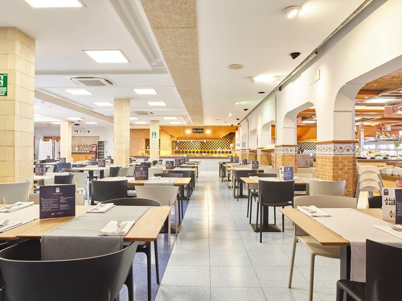 Restaurante moderno de hotel con paredes blancas, azulejos claros y filas de mesas.