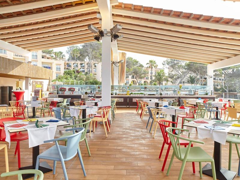 Área de restaurante abierta con sillas y mesas coloridas en terraza de madera bajo un toldo de madera.
