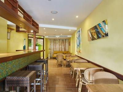 Moderní jídelní prostor s barem, stoličkami, posezením, žlutými zdmi a dřevěnou podlahou.