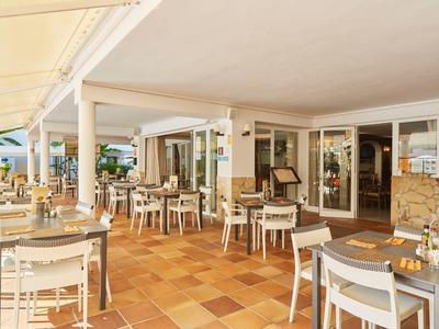 Zastřešená venkovní terasa hotelu s stolky a židlemi pro hosty.