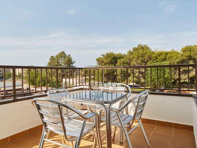 Balkon se skleněným a kovovým stolem a čtyřmi židlemi s výhledem na zelené stromy a modrou oblohu.