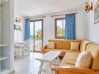 Světlý obývací pokoj se žlutou rohovou sedací soupravou, bílým nábytkem, modrými závěsy a balkonem v pozadí.