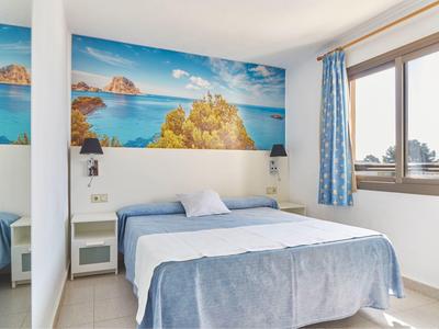 Světlo ložnice s manželskou postelí, nástěnným mořským motivem a velkým oknem s modrými závěsy.