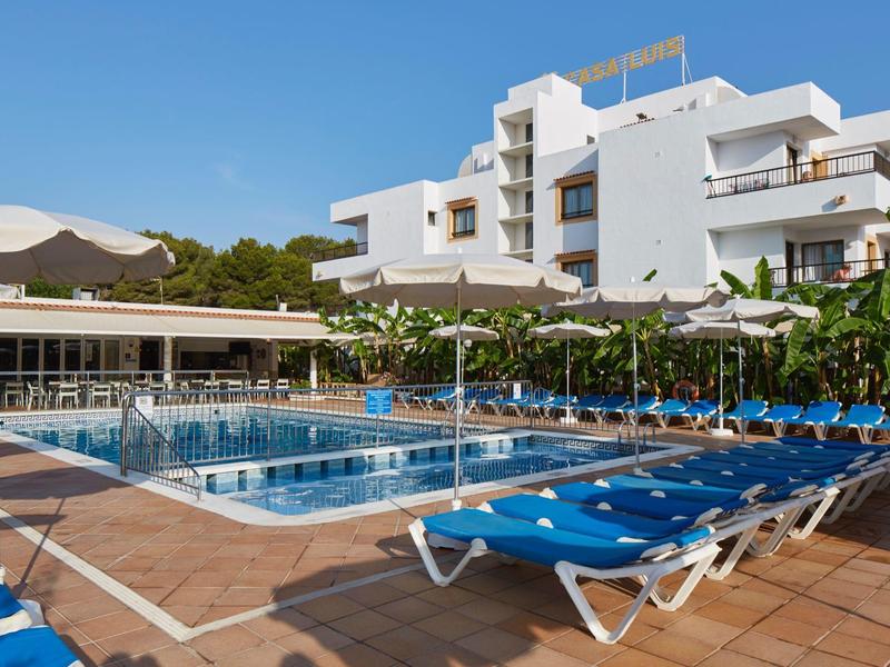 Moderní hotelový bazén s modrými lehátky a bílými budovami v pozadí.