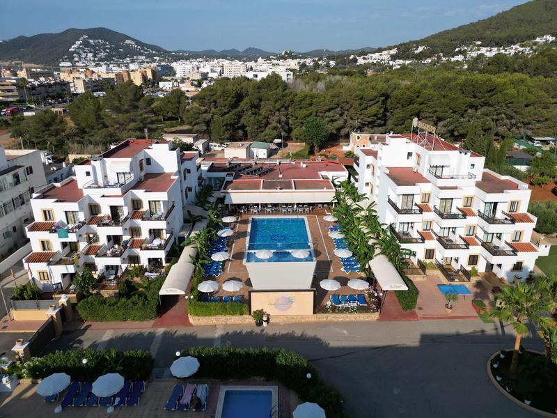 Pohled na hotel s bazénem, obklopený stromy a horami v pozadí.