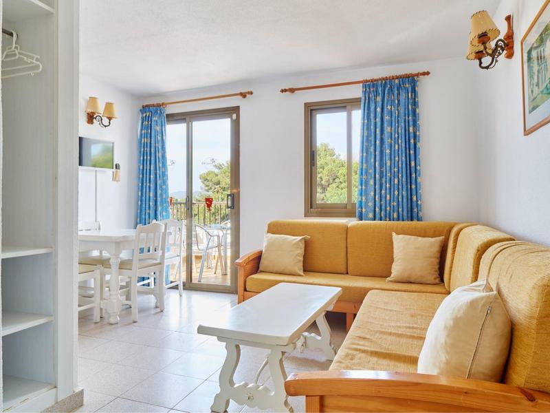 Světlý obývací pokoj se žlutou rohovou sedací soupravou, bílým nábytkem, modrými závěsy a balkonem v pozadí.