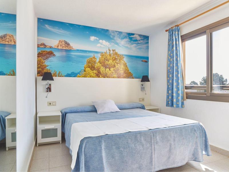 Světlo ložnice s manželskou postelí, nástěnným mořským motivem a velkým oknem s modrými závěsy.