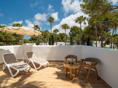 Terrasse mit Holzfußboden, zwei Liegestühlen und einem Tisch mit Stühlen vor einer weißen Mauer und Palmen.