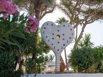 Farol decorativo en forma de corazón con recortes de estrellas en un jardín con árboles y plantas.