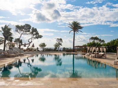 Una piscina tranquila de hotel con tumbonas y palmeras bajo un cielo despejado.