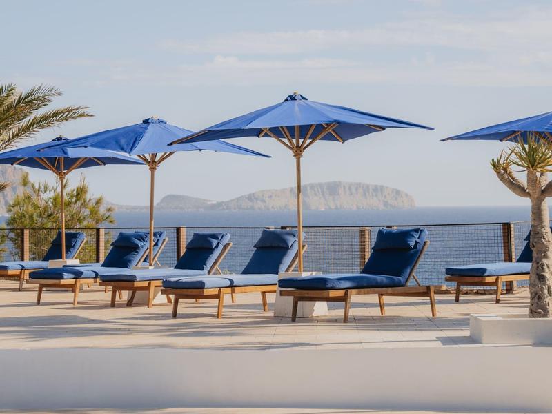 Niebieskie leżaki i parasole przy basenie z widokiem na morze i odległe wyspy.