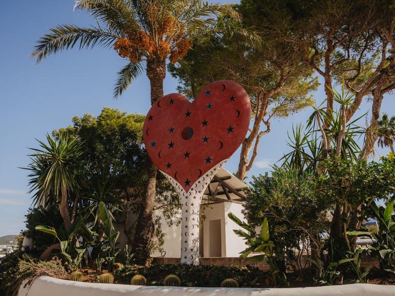 Duże czerwone serce z czarnymi kropkami jako dekoracja na zewnątrz hotelu z palmami.