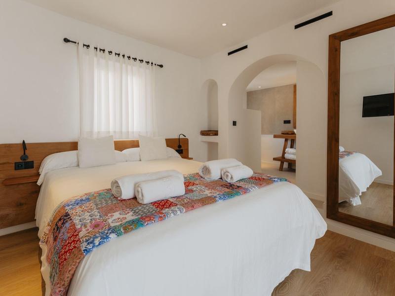 Jasna sypialnia z łóżkiem podwójnym, kolorowym narzutem i dużym lustrem na ścianie.