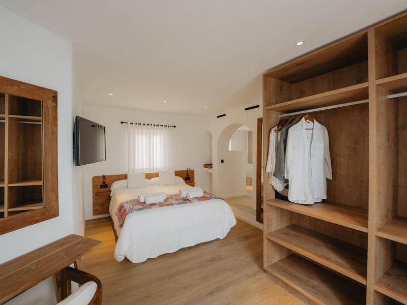 Jasna sypialnia z podwójnym łóżkiem, otwartą szafą i telewizorem na ścianie.