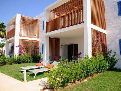 Nowoczesny hotel z balkonami, leżakami i zielonymi roślinami z przodu.