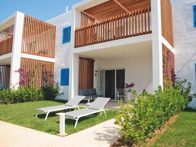 Modernes Ferienhaus mit Balkon und Terrasse, umgeben von Grünflächen und Liegestühlen.