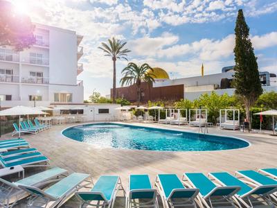 Moderner Außenpool mit türkisfarbenen Liegestühlen, Palmen und hellem Gebäude bei Sonnenschein.