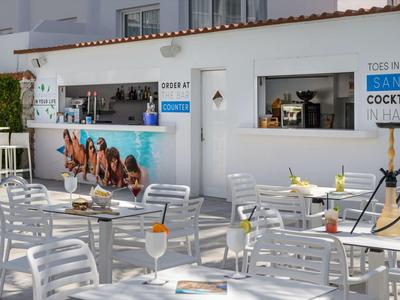 Strefa baru na zewnątrz z białymi stołami i krzesłami oraz fajką wodną do palenia.