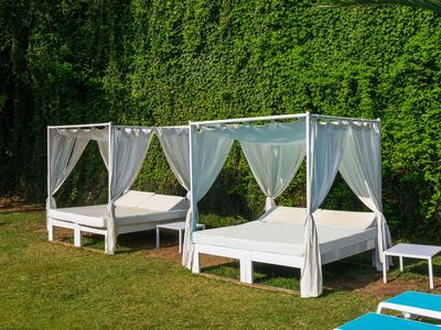 Deux lits à baldaquin blancs avec des rideaux sur une pelouse devant une haie verte.