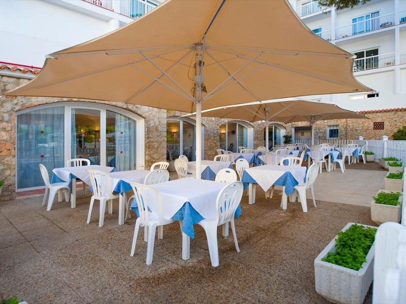 Restauracja na świeżym powietrzu z białymi stołami i niebieskimi krzesłami pod dużymi parasolami.