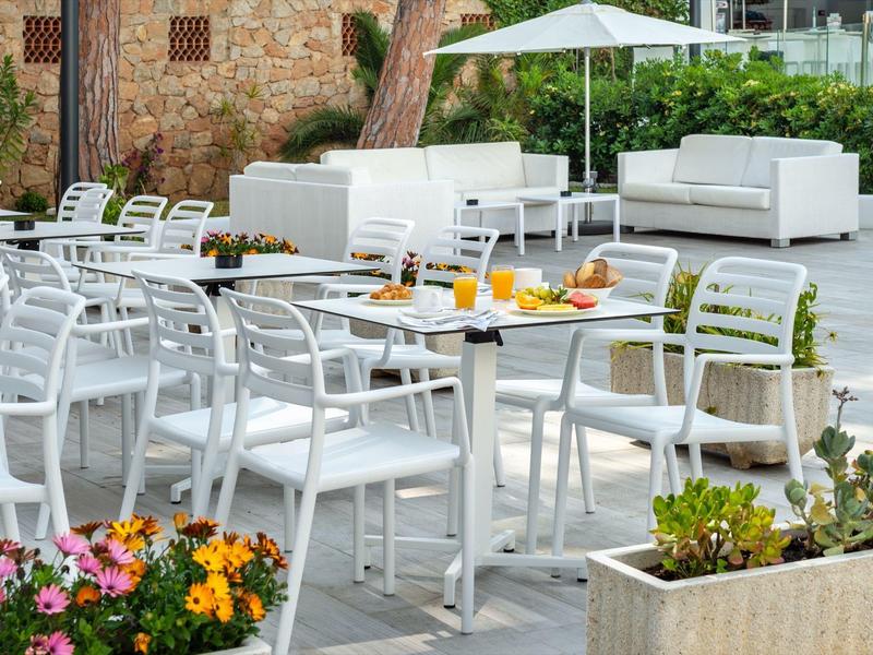 Nowoczesna przestrzeń na zewnątrz z białymi krzesłami i stolikami, parasolem i doniczkami z roślinami.