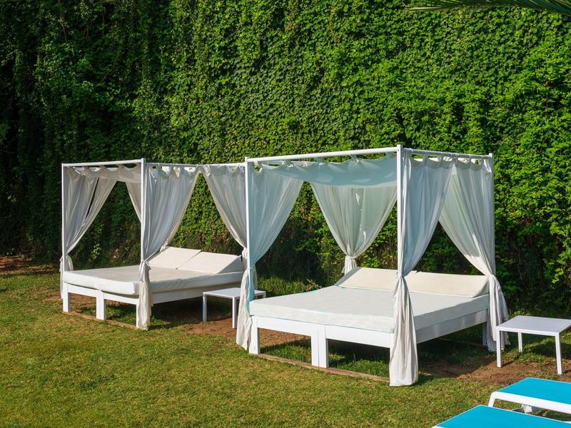 Dwa białe łóżka z baldachimem z zasłonami na trawniku przed zielonym bluszczem.