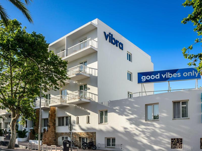 Nowoczesny biały budynek hotelu z widocznym napisem i niebieską tablicą 'good vibes only'